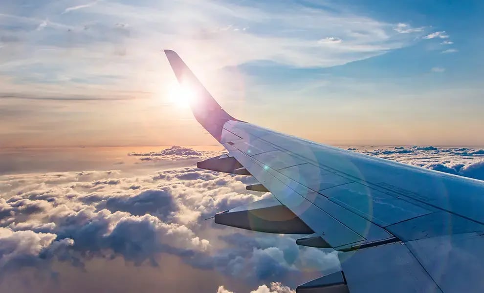 Vy från flygplansfönster med vinge ovanför moln i soluppgång, som symboliserar resa och överblick.