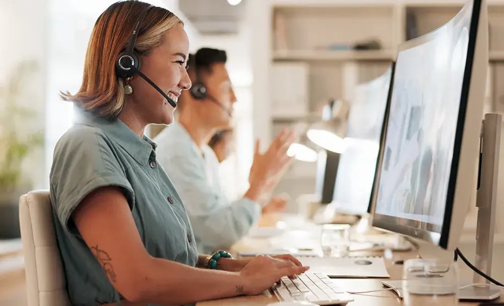 Personer som arbetar vid sina datorer i en modern kontorsmiljö, med headset på, redo att ge professionell och personlig kundservice.