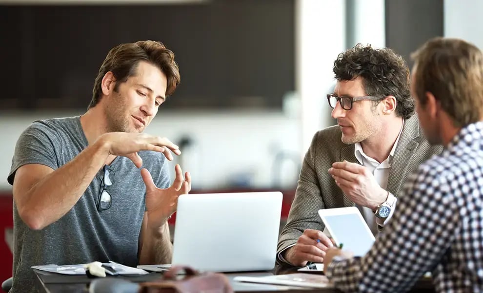 Personer som diskuterar idéer under ett arbetsmöte vid ett bord med laptop och dokument.
