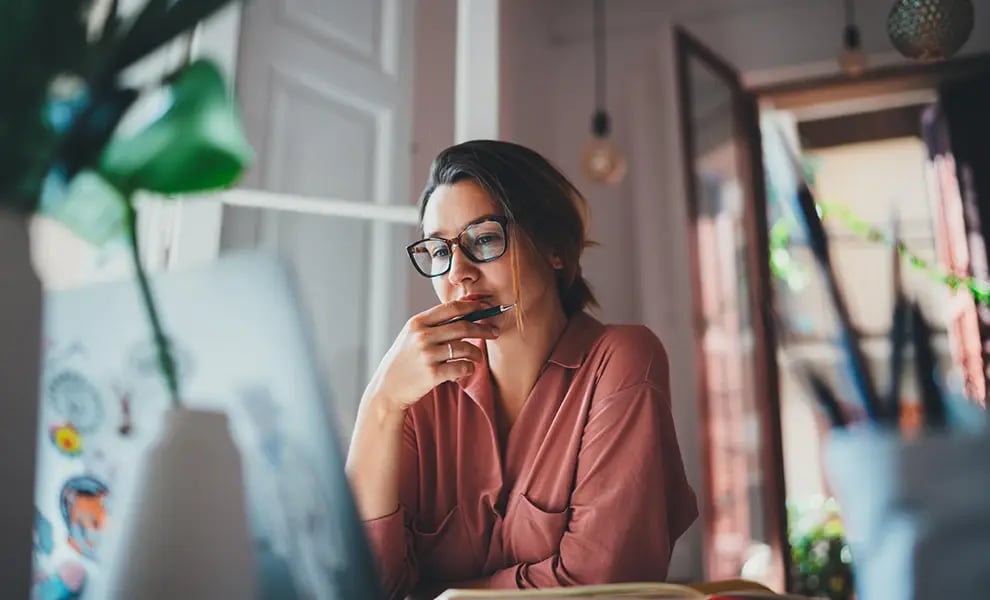 Kvinna med glasögon sitter vid dator i hemmiljö och planerar tjänsteresa.