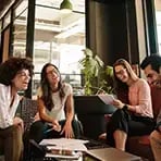 En grupp personer sitter tillsammans i ett modernt kontor och arbetar i ett möte, med dokument och dator framför sig.